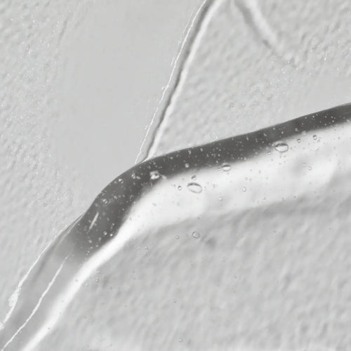 Nahaufnahme von Solawaves LightBoost Wand Activating Serum, einem klaren Gel mit Hyaluronsäure. Es zeigt Luftblasen vor einem strukturierten weißen Hintergrund, der die glatte, glänzende Oberfläche im Kontrast zum rauen Hintergrund hervorhebt.