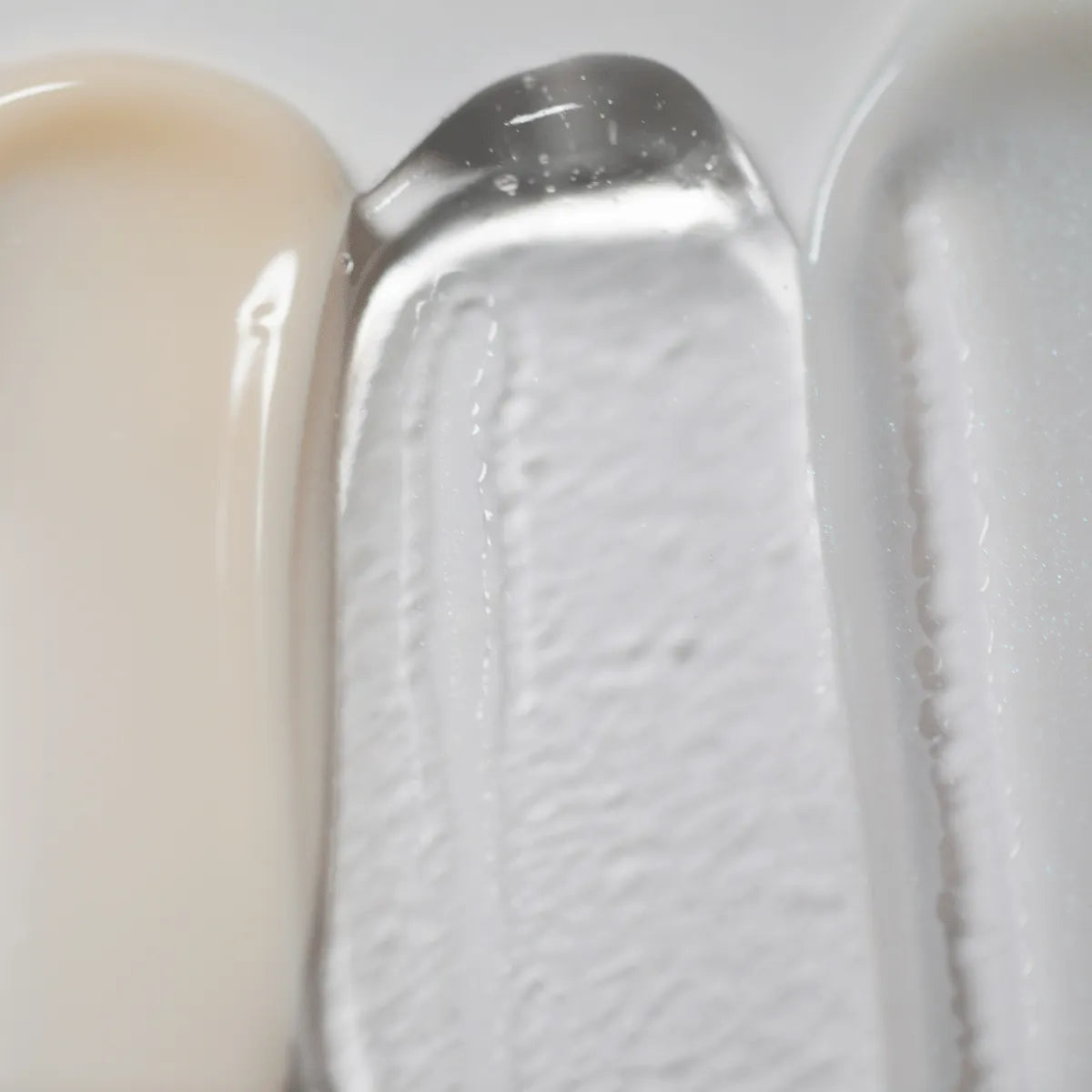 Eine Nahaufnahme zeigt die Texturen des Solawaves LightBoost Wand Activating Serum: cremiges Beige, transparentes Gel mit LightBoost-Technologie und glatte hellgraue/weiße Creme. Die Texturen reichen von cremig bis gelartig und weisen jeweils ein glänzendes Finish auf.